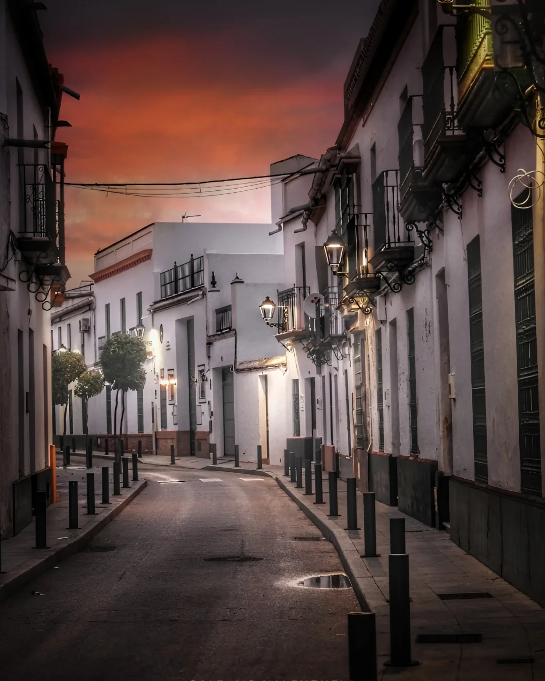Una calle tranquila de Umbrete al anochecer, con farolas encendidas iluminando el camino.