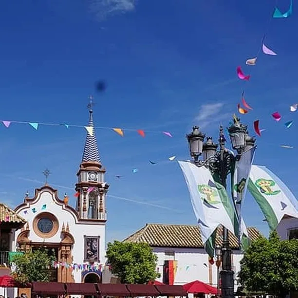 Calles de Cañada Rosal en fiestas, adornadas con banderines coloridos en farolas y edificios, con una iglesia de fondo.