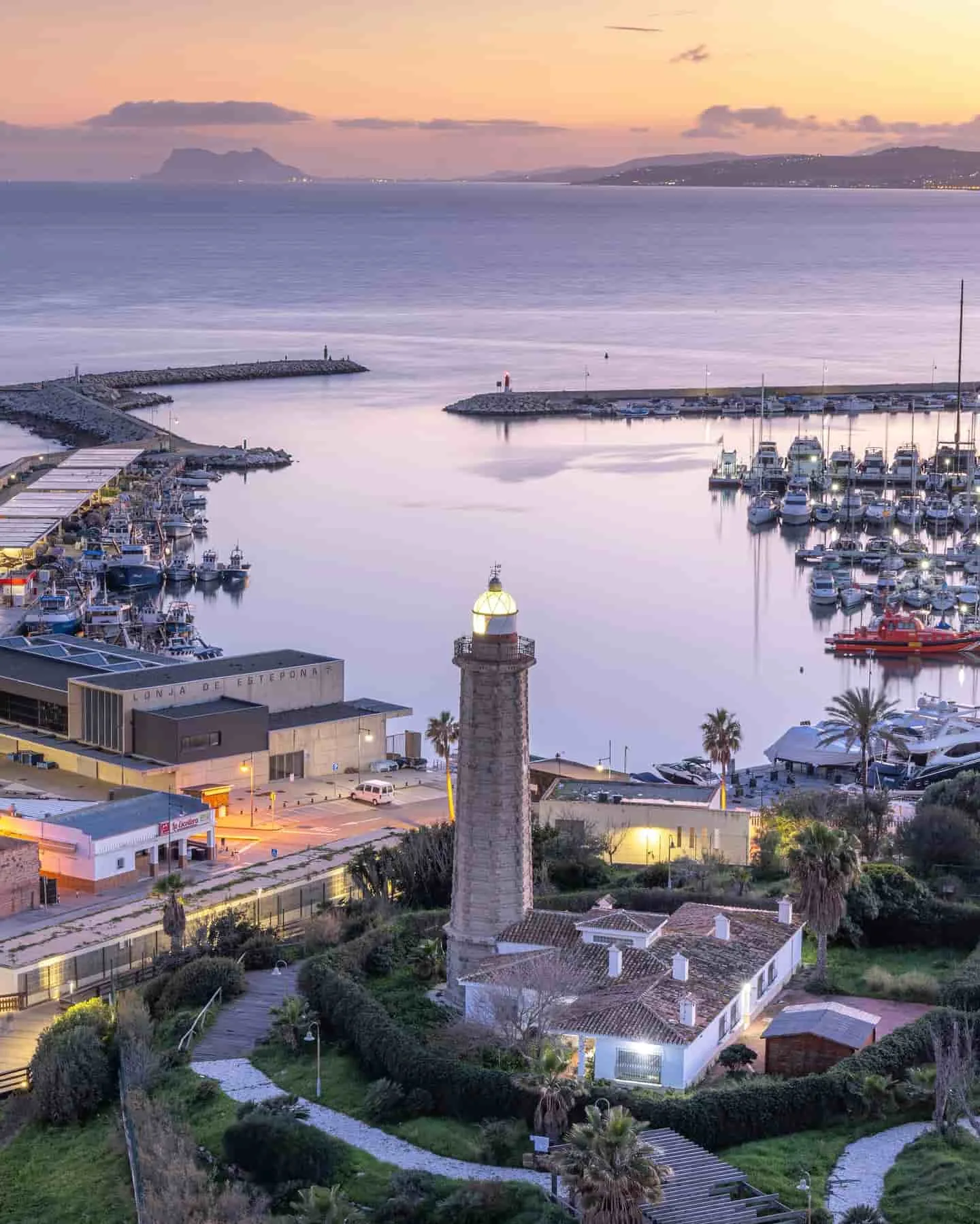 Vistas del faro y el puerto marítimo de Estepona iluminados por la luz del atardecer.
